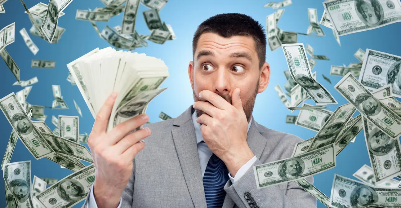 Ein Mann im Anzug hält einen Haufen Geld in der Hand, umgeben von fliegenden Hundert-Dollar-Scheinen, die den unerwarteten Reichtum der Ultra High Net Worth Individuals (UHNWI) symbolisieren.