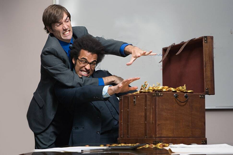 Two business professionals in a physical struggle over a treasure chest filled with gold coins, symbolizing the conflict in compensation models for wealth management.
