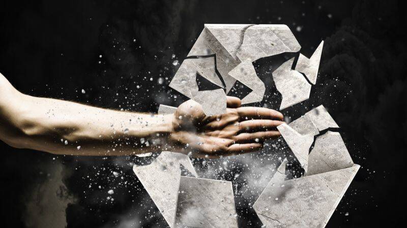 Eine Hand zerschlägt ein Recycling-Symbol aus Beton, das für die Herausforderungen im Bereich ESG-Vermögensverwaltung und Nachhaltigkeit steht.