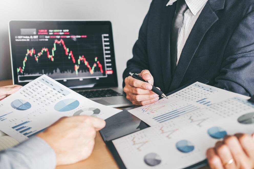 Geschäftsleute, die ihre Anlageportfolios anhand von Finanzdiagrammen und Börsendaten auf einem Laptop überprüfen.
