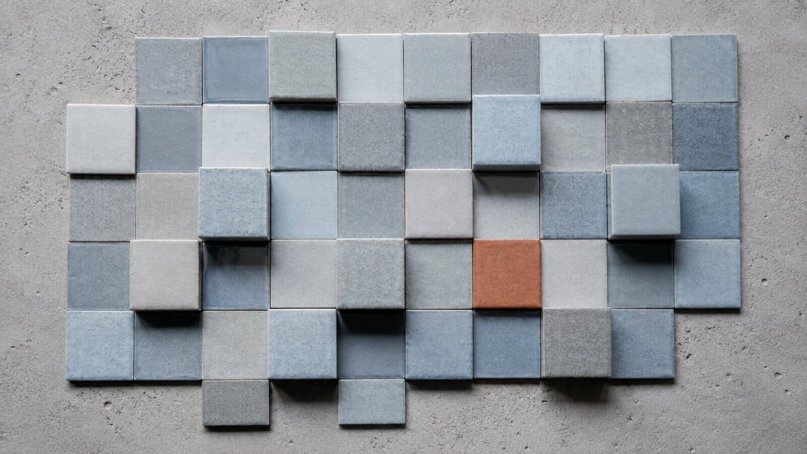 Uneven grid of ceramic tiles in grey and blue with one terracotta tile — a visual metaphor for comparing what AI costs independent wealth managers