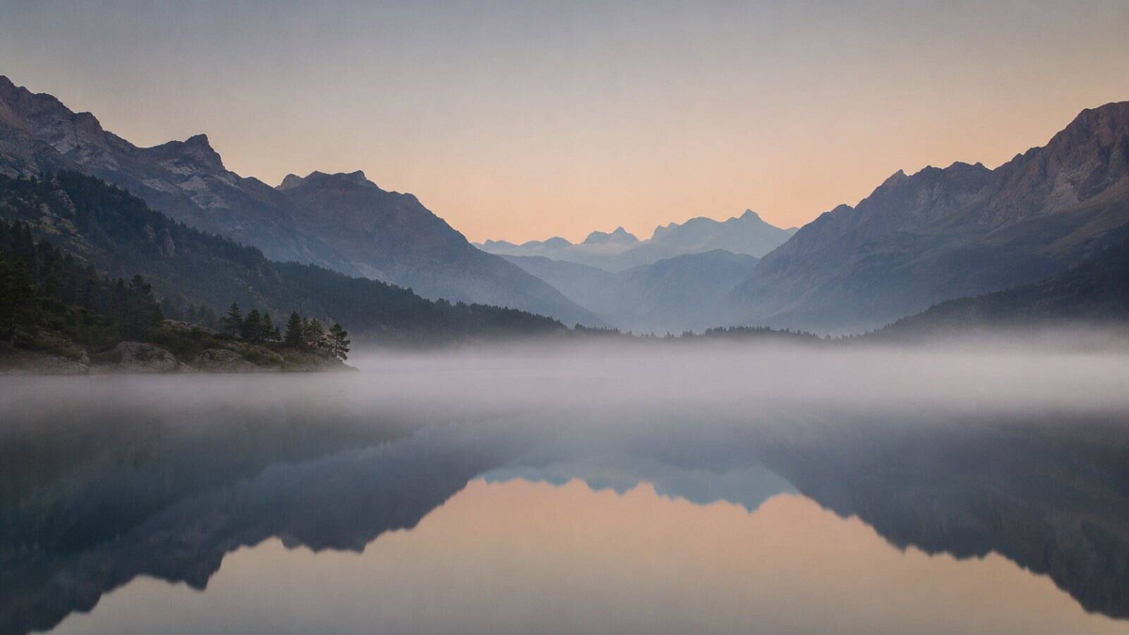 Ruhiger Alpensee in der Schweiz im Morgengrauen mit Nebel über dem Wasser